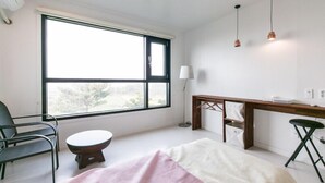 Une chambre moderne avec une grande fenêtre, un bureau, une chaise et une table de chevet.