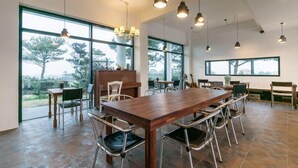 Un vaste espace dédié à la salle à manger, avec une grande table et des chaises en bois, de grandes fenêtres donnant sur la verdure et un éclairage suspendu.