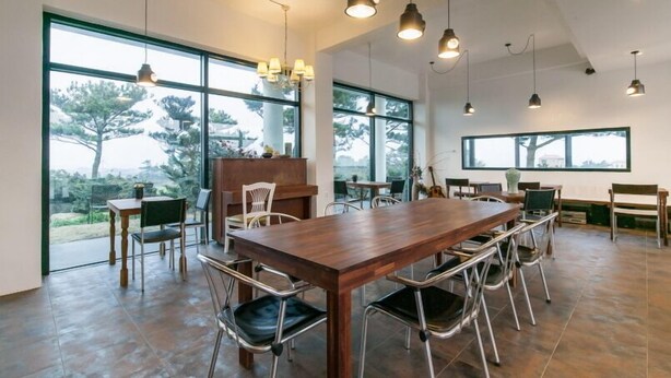 Un vaste espace dédié à la salle à manger, avec une grande table et des chaises en bois, de grandes fenêtres donnant sur la verdure et un éclairage suspendu.