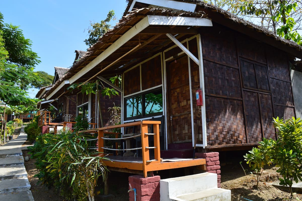 A wooden house with a thatched roof, a wooden porch, and a brick foundation.