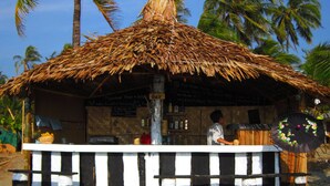 Eine Strandhütte mit einem Reetdach, einem schwarz-weiß gestreiften Unterbau und einem Schild, das birmanisches Bier und andere Getränke anbietet.