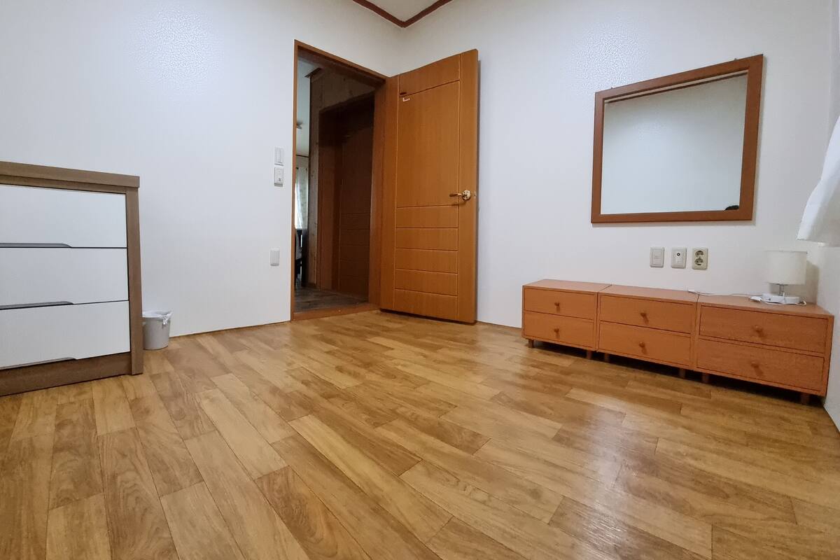 Ein Zimmer mit Holzboden, einem weißen Kleiderschrank, einem Holzschrank und einem Spiegel an der Wand.