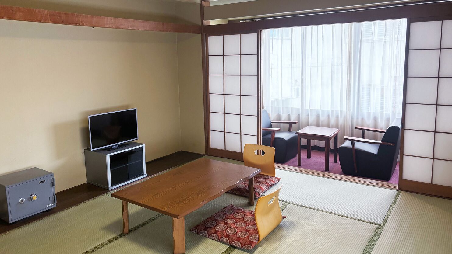 A traditional Japanese room with tatami flooring, a low wooden table, a television, and sliding doors leading to a balcony.