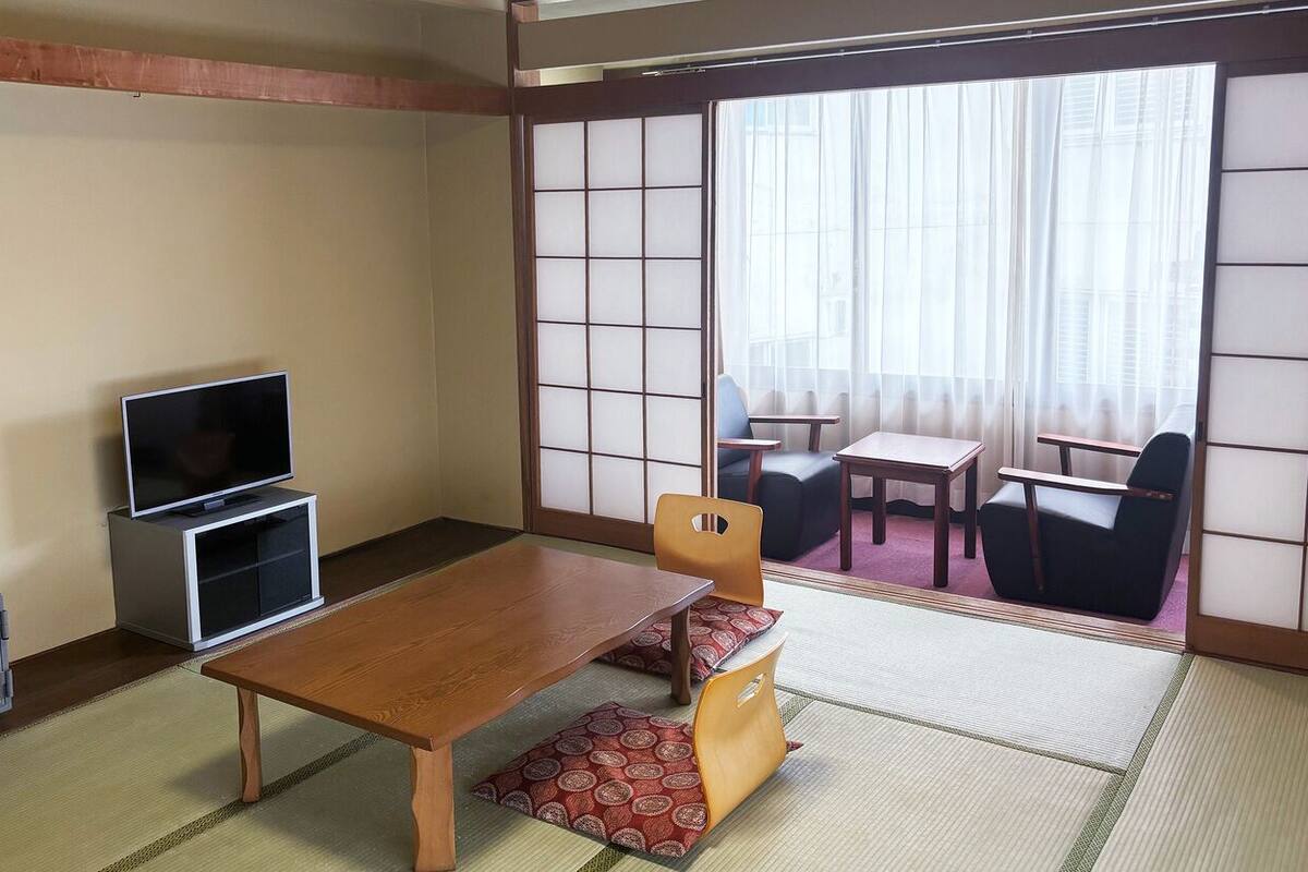 A traditional Japanese room with tatami flooring, a low wooden table, a television, and sliding doors leading to a balcony.