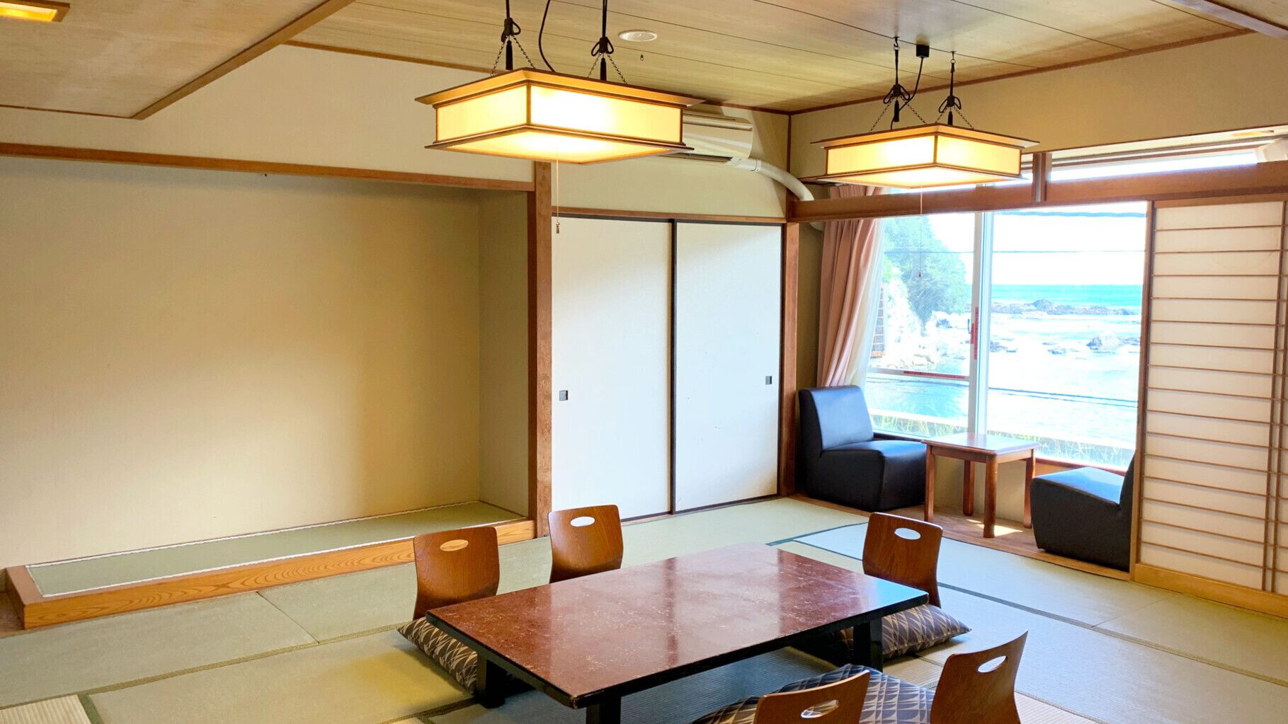 A traditional Japanese room with tatami flooring, a low table, and a view of the sea.