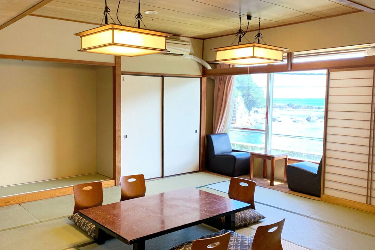 A traditional Japanese room with tatami flooring, a low table, and a view of the sea.