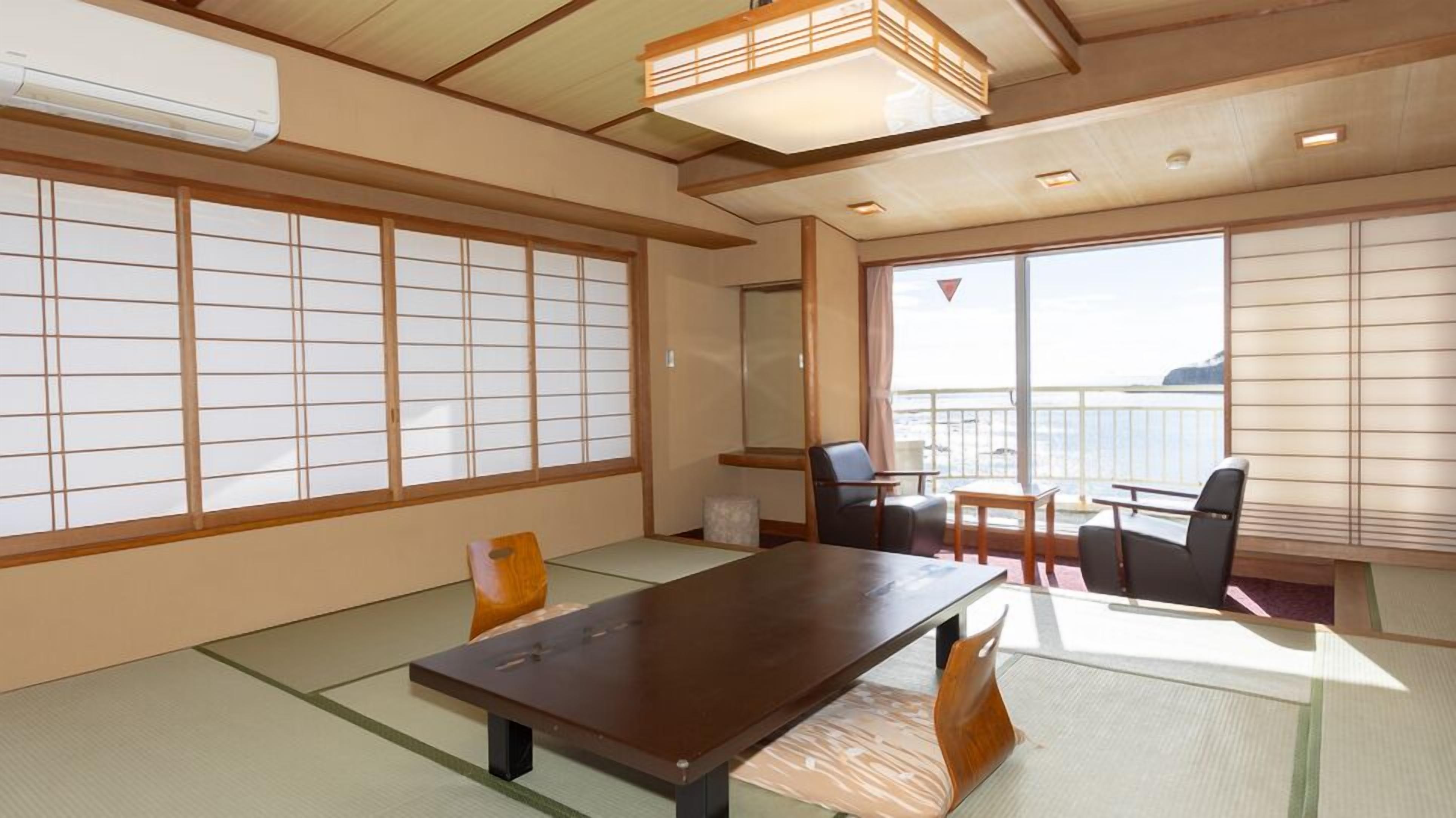 A traditional Japanese room with tatami flooring, a low table, chairs, a sliding door, and a view of the sea.