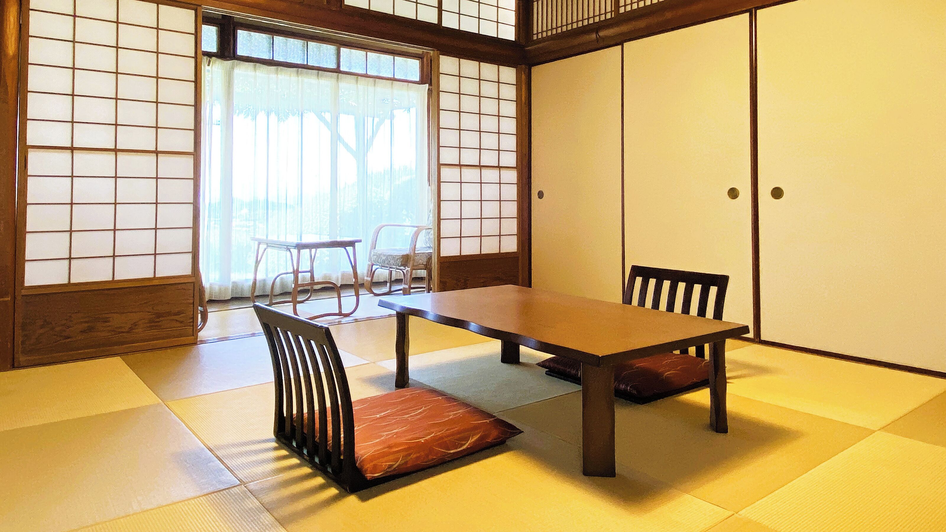 A tatami mat room with a low table and chairs, a sliding door, and a view through a shoji screen.