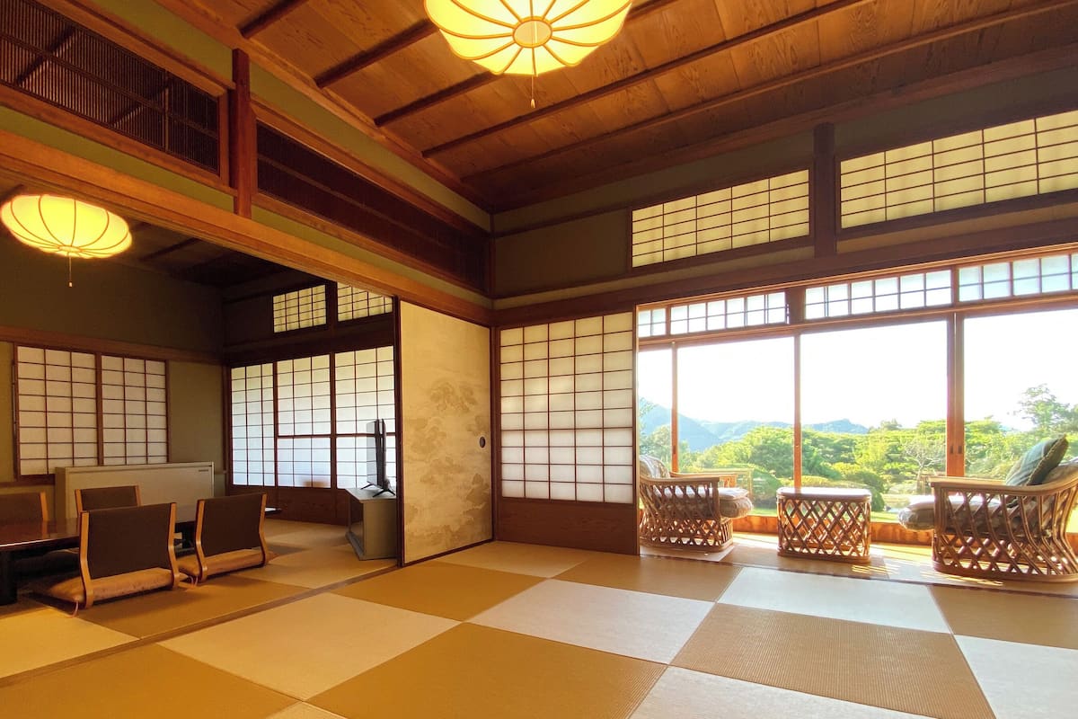 Una habitación japonesa tradicional con suelo de tatami, puertas correderas y vistas a la montaña.