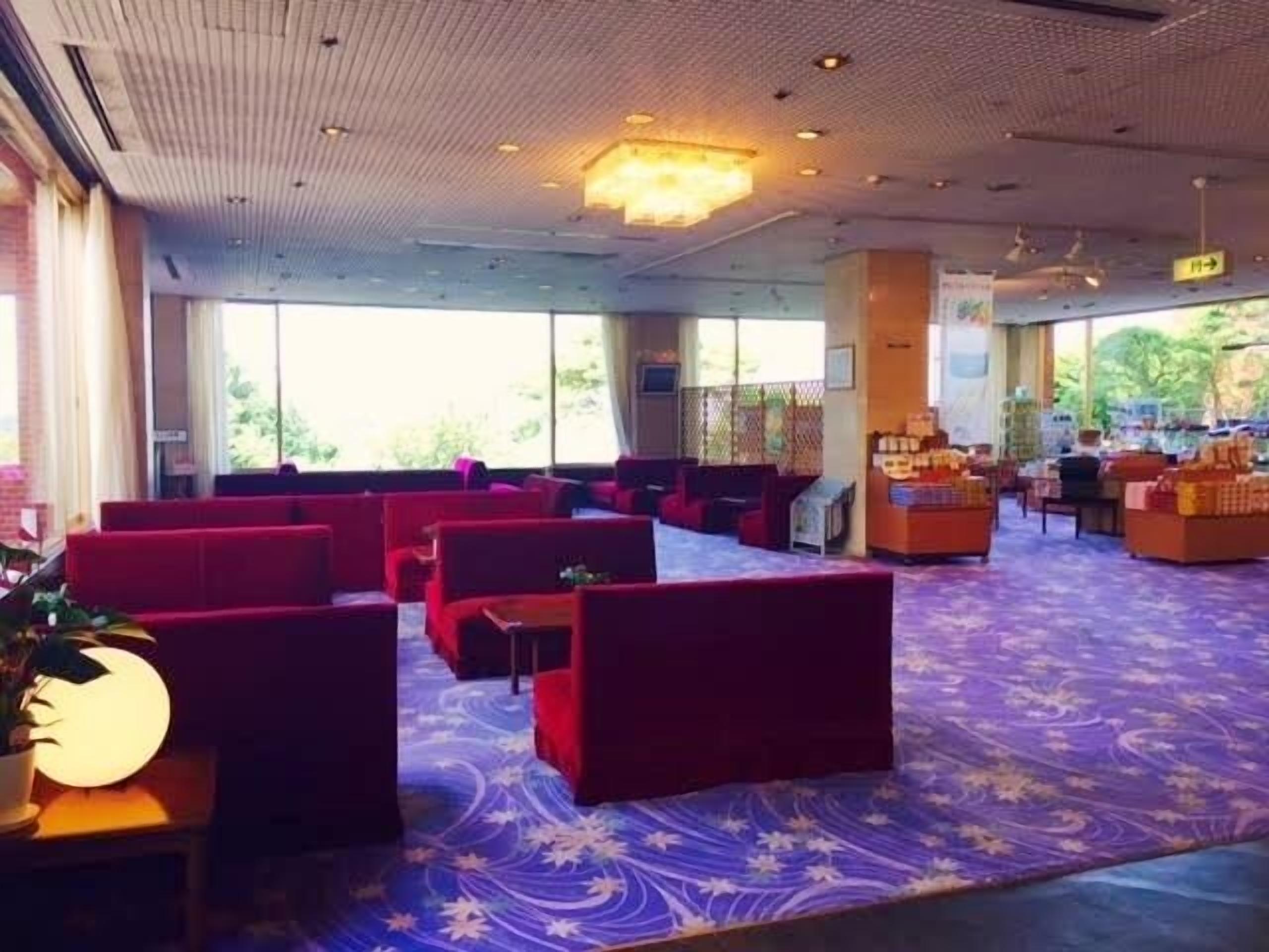 Un hall d’entrée spacieux, doté de sièges rouges, d’un tapis à motifs et de grandes fenêtres offrant une vue sur la verdure.