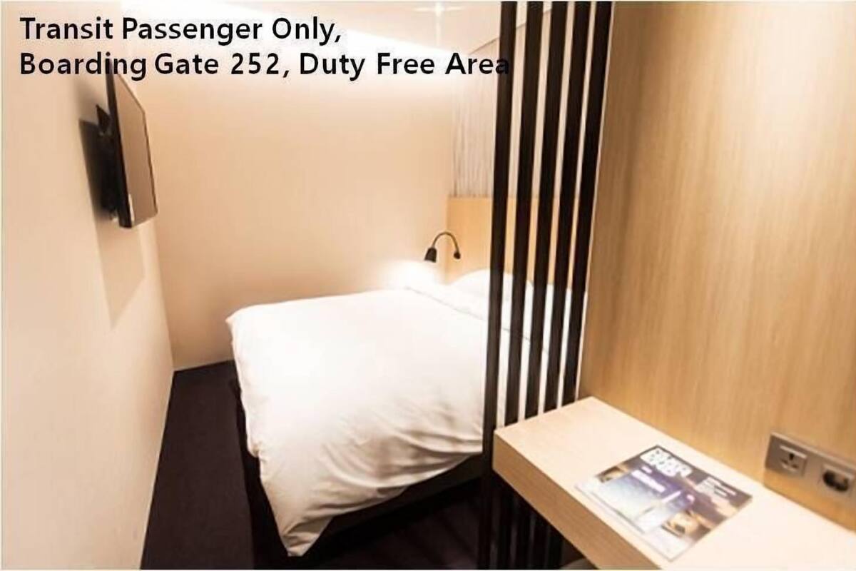 A small, single-bed room with a bed, a nightstand, and a wall-mounted TV.