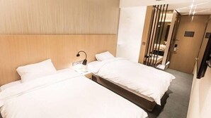 A hotel room with two single beds, a bedside table with a lamp, and a door leading to a bathroom. - Incheon Airport Transit Hotel - Terminal 2 (Incheon)