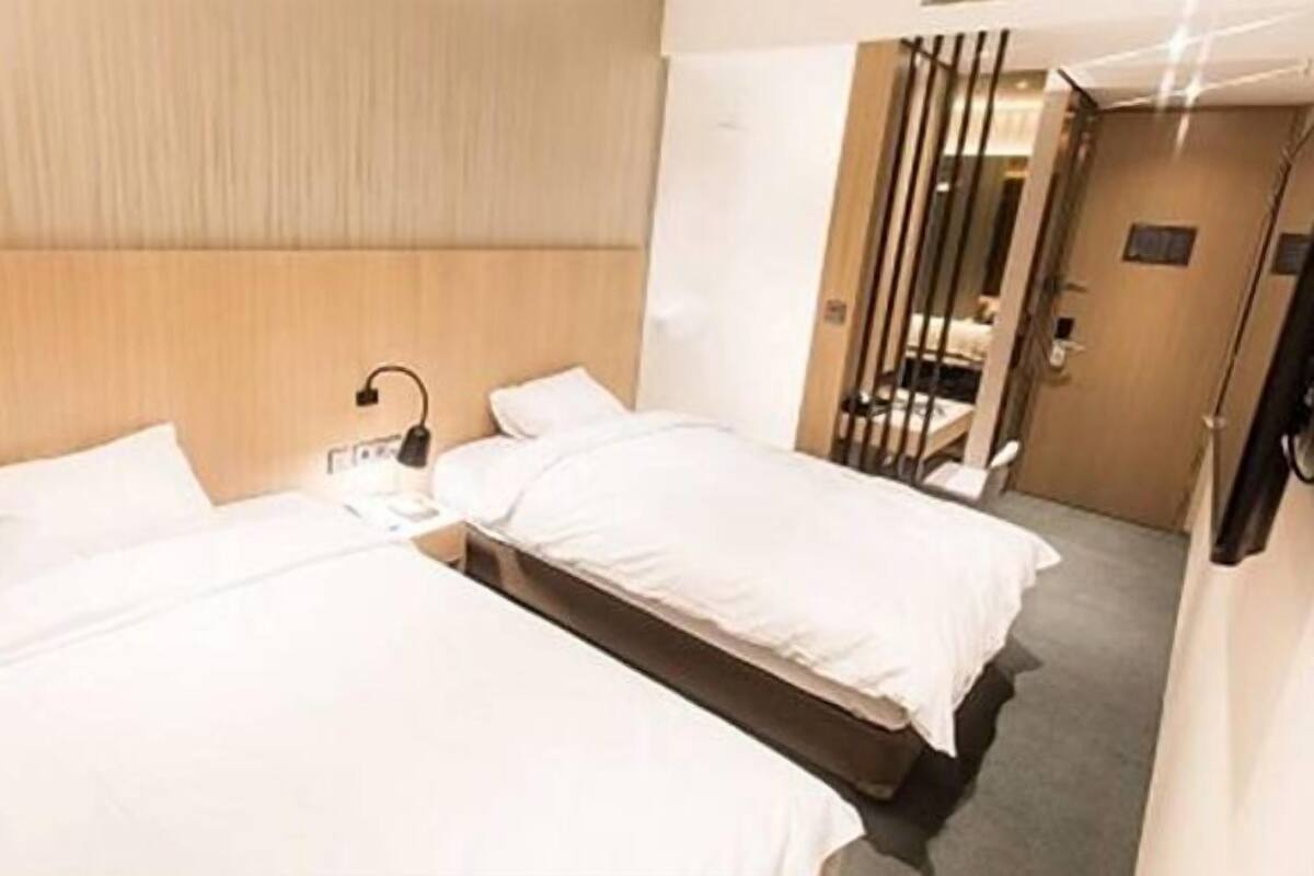 A hotel room with two single beds, a bedside table with a lamp, and a door leading to a bathroom.