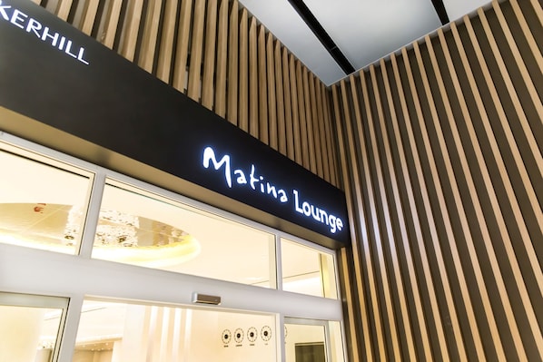 En skylt med texten ”Matina Lounge” ovanför en byggnads entré, där fasaden är klädd med vertikala träpaneler.
