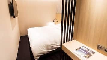 A small, neatly arranged hotel room with a bed, a bedside table, and a wall-mounted light.