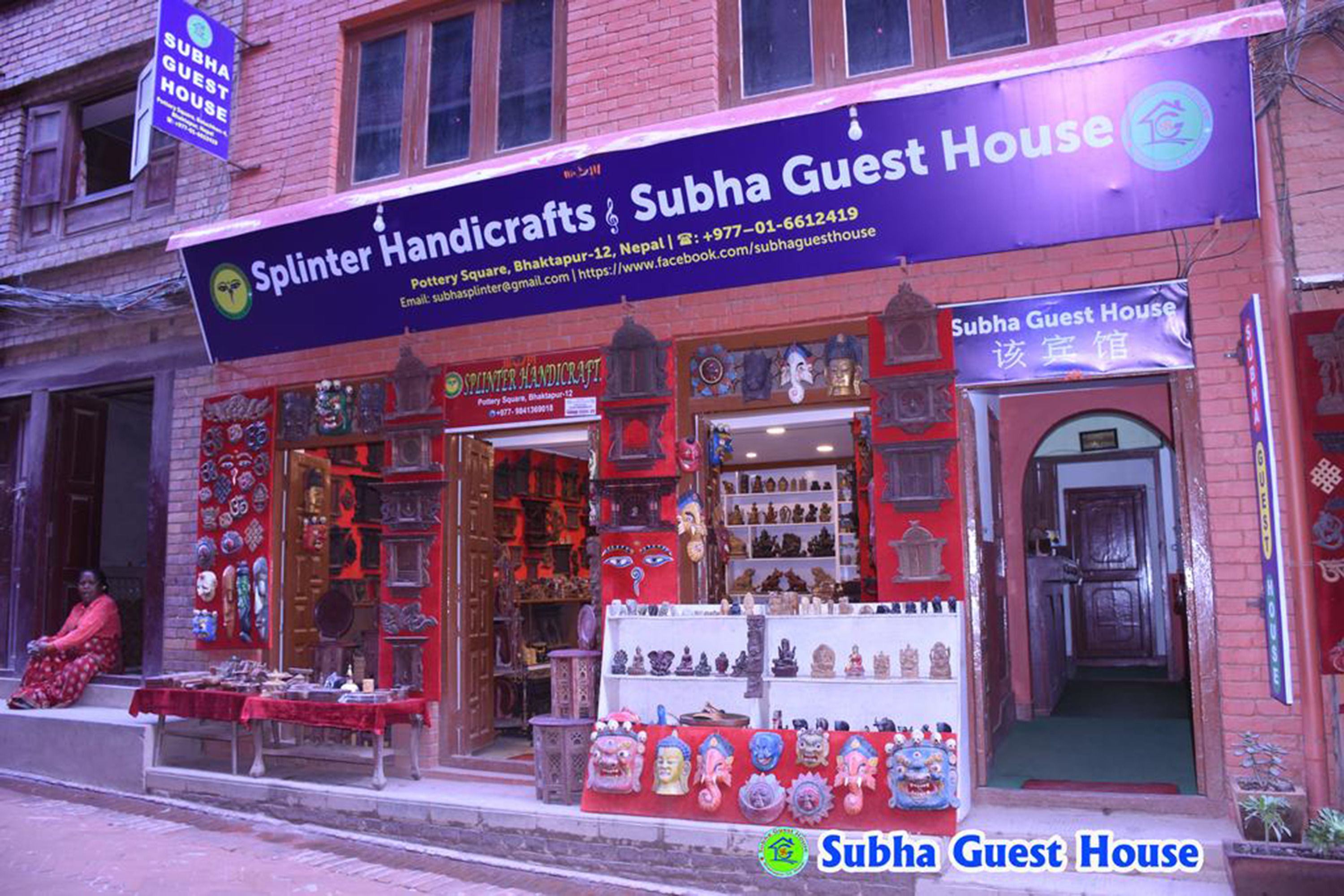 A brick building with a sign for 'Splinter Handicrafts & Subha Guest House' displaying various items for sale.