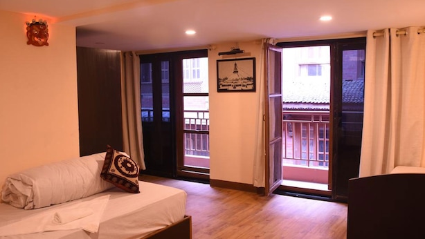 Habitación de hotel con cama, ventana con vista a edificios y puerta que da a un área exterior.