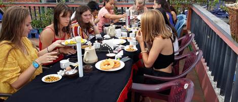 Un grupo de personas cenando en una mesa al aire libre, con diferentes platos y bebidas.