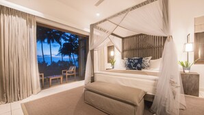 A bedroom with a bed, a canopy, a view of palm trees, a window with curtains, a bedside table with a lamp, and a small table with chairs. - Kumu Beach (Balapitiya)