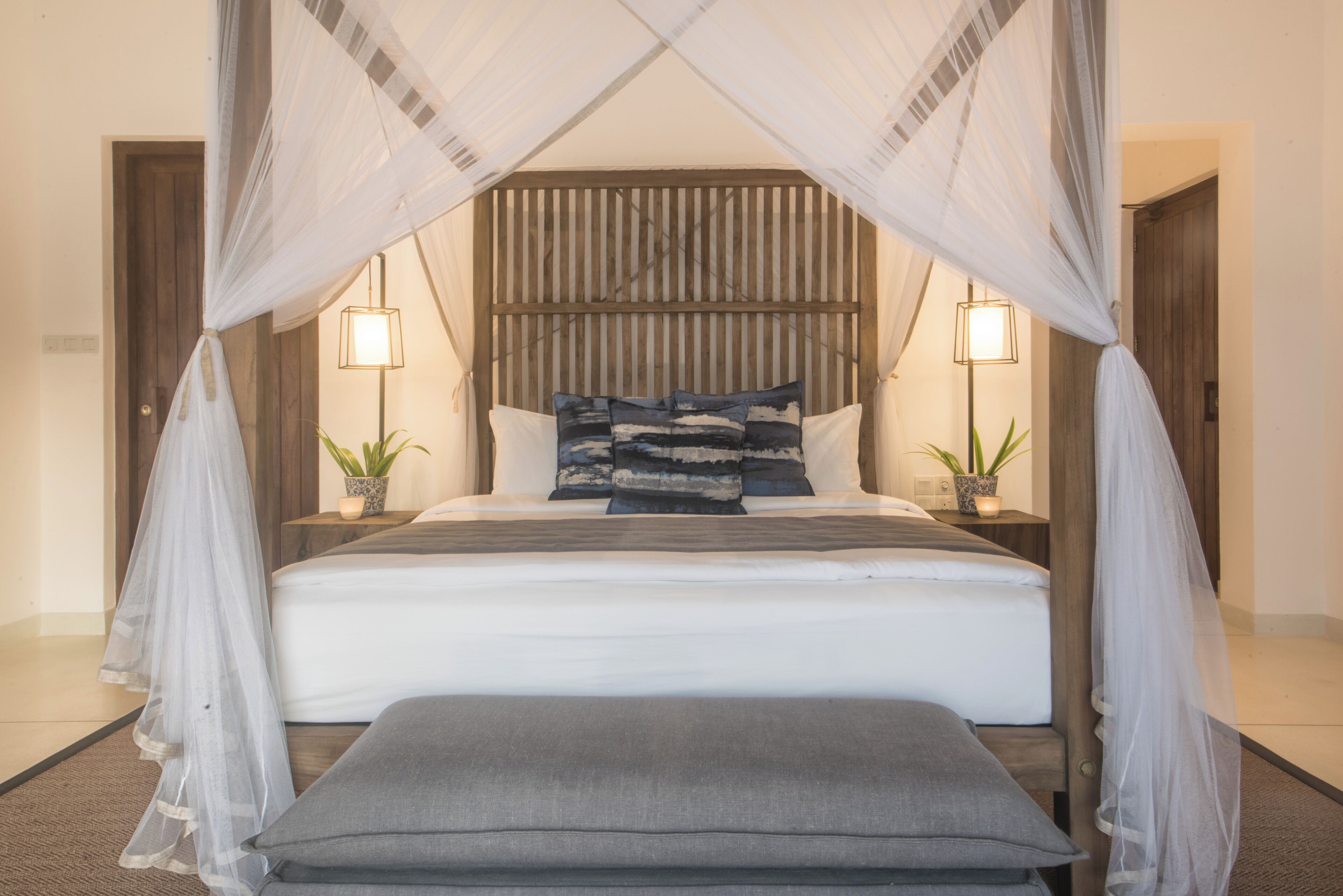A bedroom with a canopy bed, bedside lamps, and two potted plants.