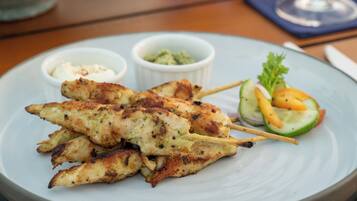 A plate of grilled chicken skewers with a side salad and a glass of white wine on a wooden table.