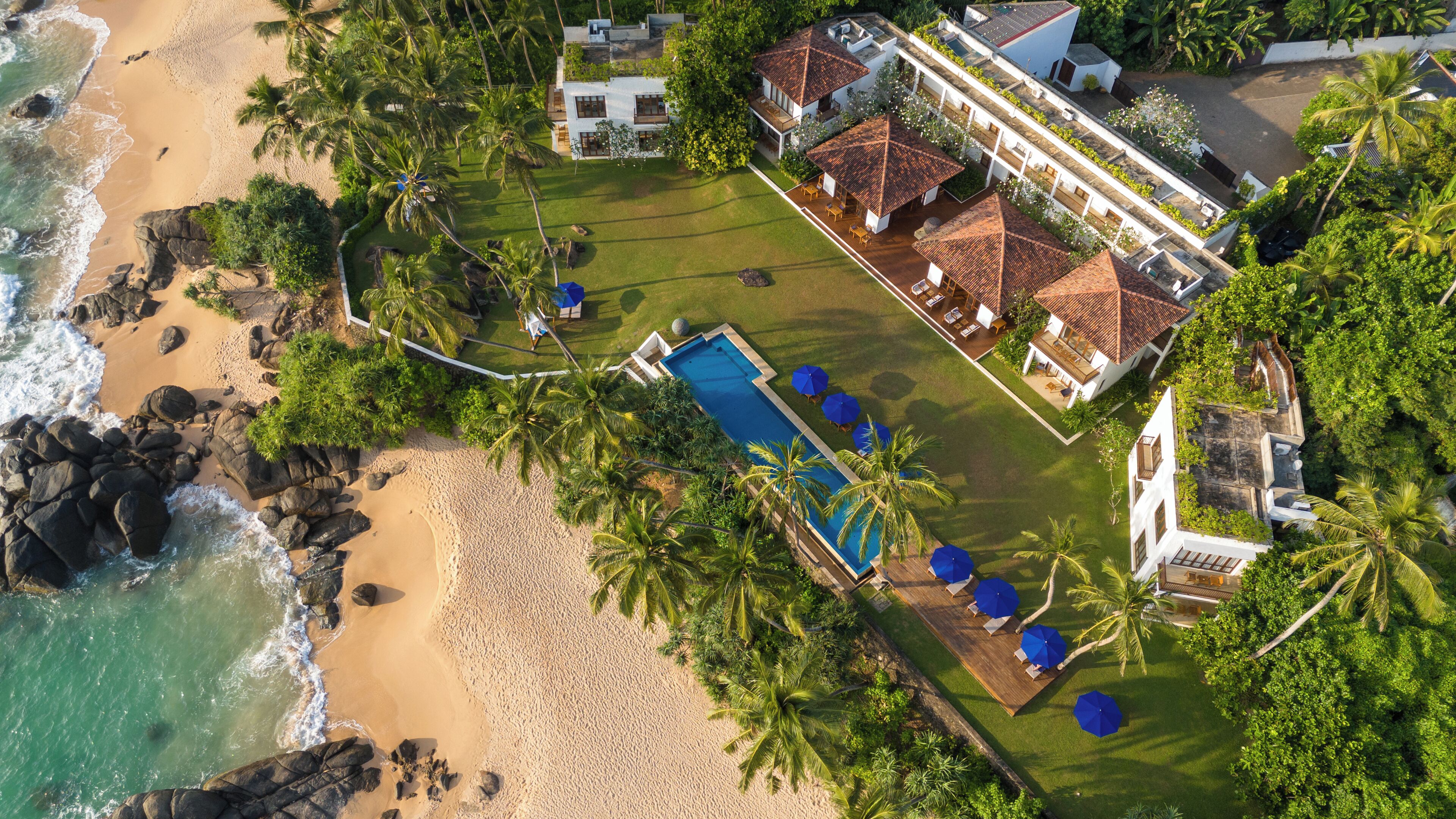 Vista aérea de una propiedad frente a la playa, con piscina, zona de estar y un amplio jardín.