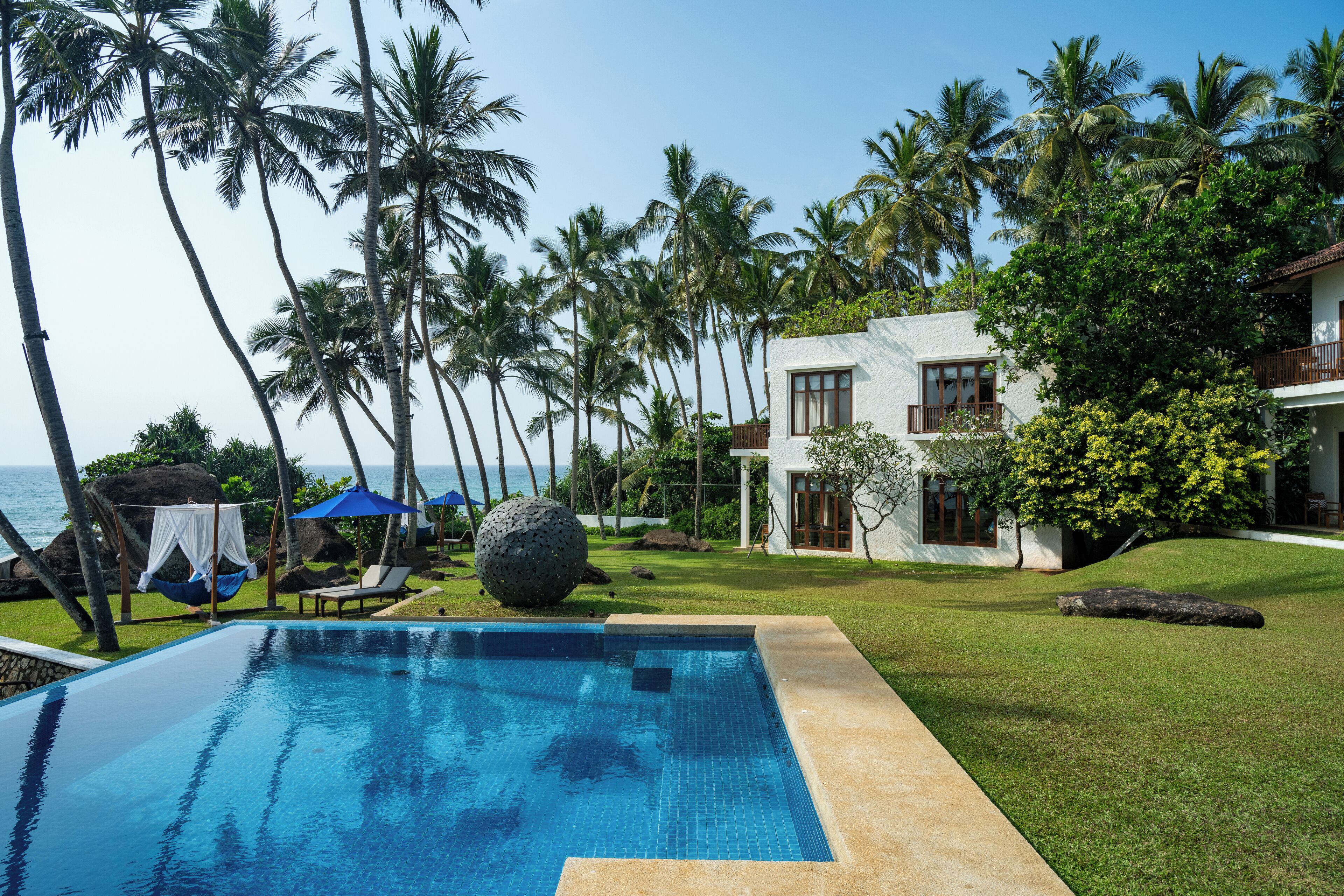 A pool with clear blue water, surrounded by a well-maintained lawn and palm trees.