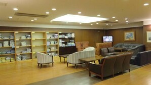 A spacious lobby with wooden flooring, multiple seating areas including sofas and chairs, and shelves with folded items. - Itoen Hotel Atamikan (Atami)