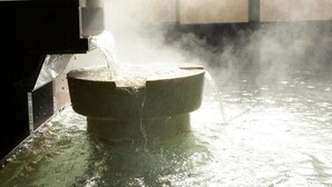 A toilet in a room with a large window, water flowing from the tank into the bowl, and steam rising from the water. - Itoen Hotel Atamikan (Atami)