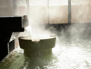 A toilet in a room with a large window, water flowing from the tank into the bowl, and steam rising from the water.