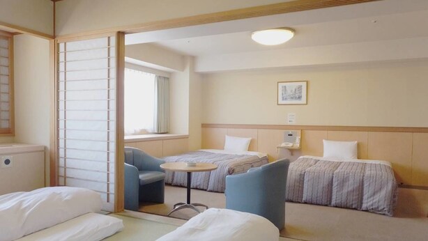A hotel room with two beds, a small table, and a chair. - Itoen Hotel Atamikan (Atami)