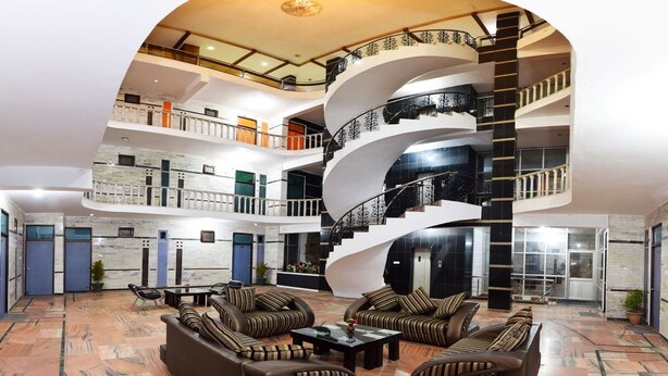 A multi-level atrium with a central staircase, seating area with striped sofas, and a marble floor. - Hotel President (Dalhousie)