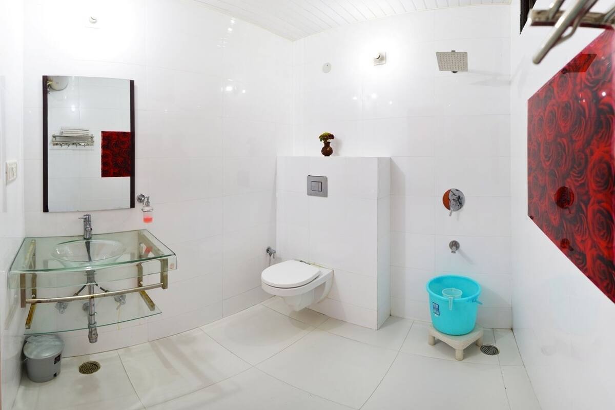 Un baño con lavamanos de vidrio, inodoro blanco y un balde azul.