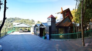 A hotel entrance with a covered walkway, a mountain backdrop, and a restaurant with a sign. - Hotel President (Dalhousie)