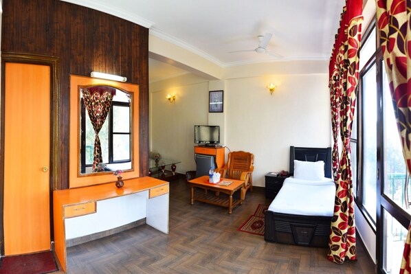 Habitación de hotel con cama, escritorio, silla, televisor y ventana con cortinas.