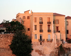 A multi-story building with balconies, a stone wall, and trees. - Dorothy's Dream (Chania)