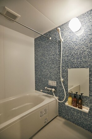 A modern bathroom with a white bathtub, a shower head, and a tiled wall. - Pinn-S4E5 (Sapporo)