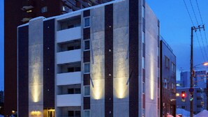 A multi-story building with a modern architectural design, featuring balconies and illuminated windows.