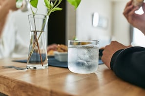 A wooden table with a glass of water and a vase with a plant. - Pinn-S4E5 (Sapporo)