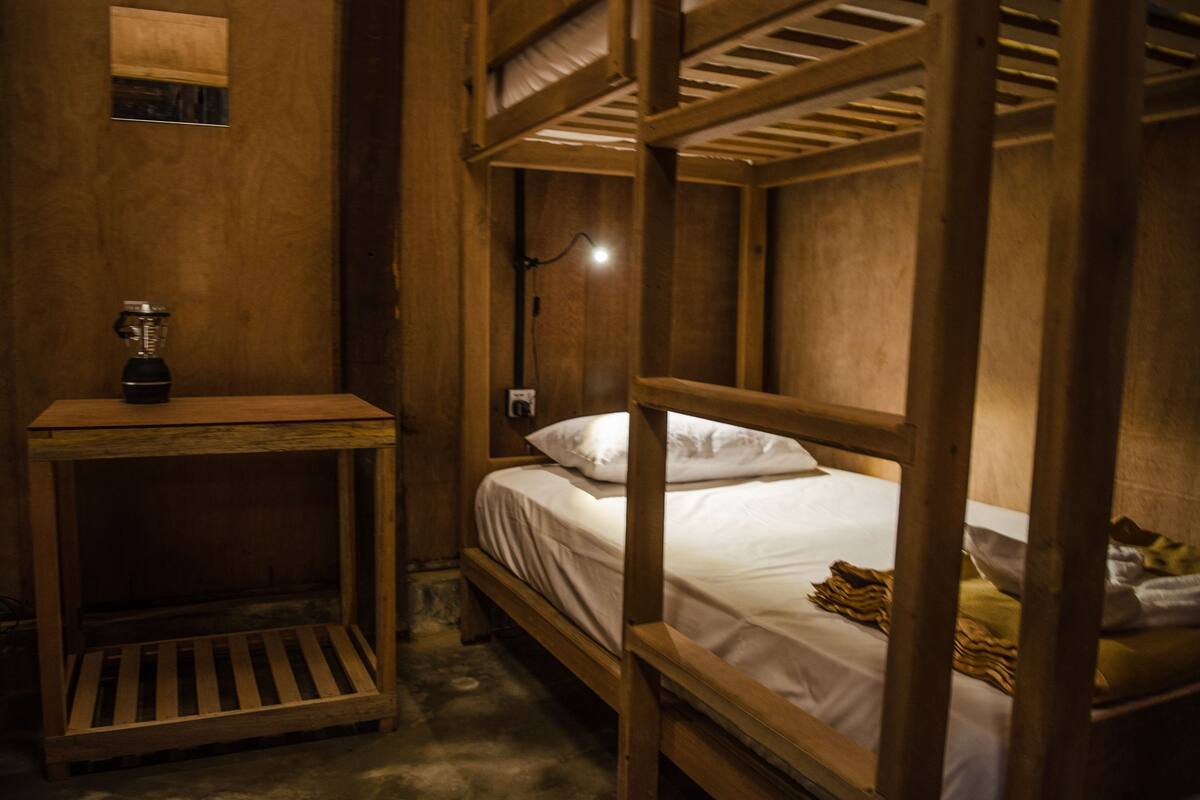 A bunk bed room with a wooden headboard, a small table with a blender, and a single light fixture.