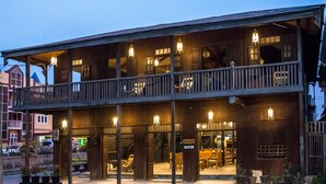 A two-story wooden building with a balcony, multiple windows, and outdoor seating. - Hardwood Lodge - Hostel (Nyaungshwe)