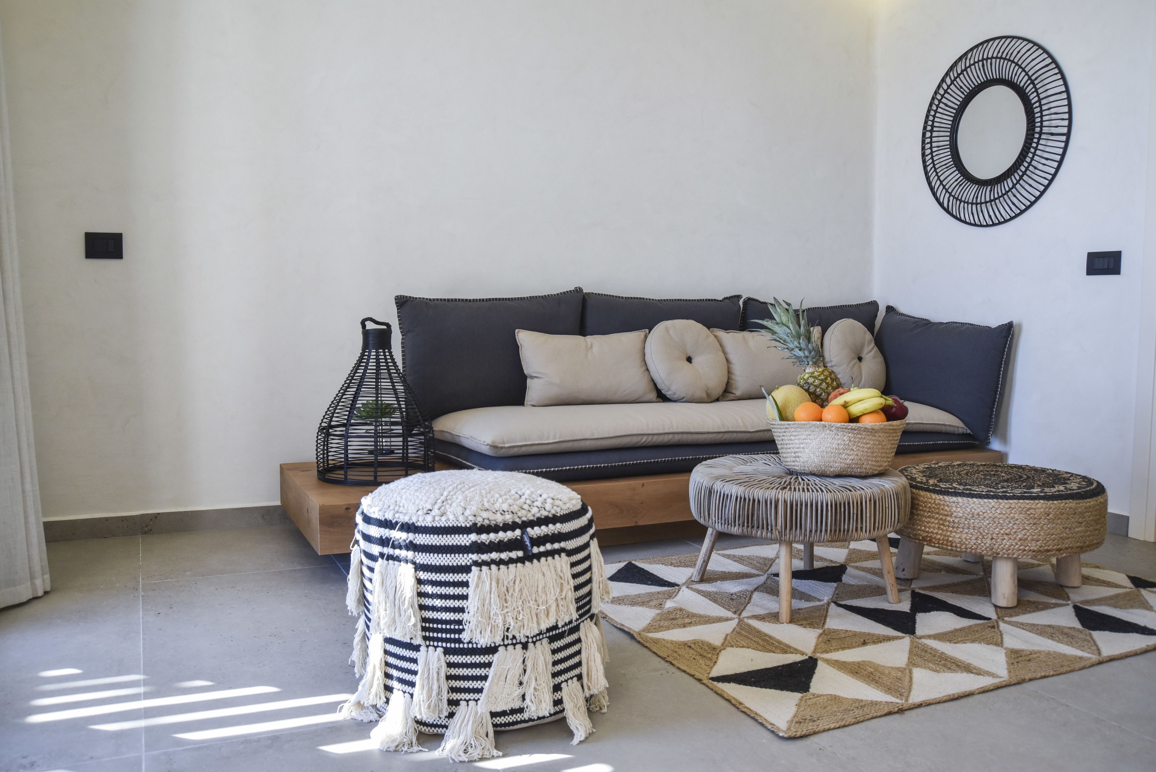 Un salon moderne avec un canapé, des poufs, un panier de fruits et un tapis à motifs géométriques.