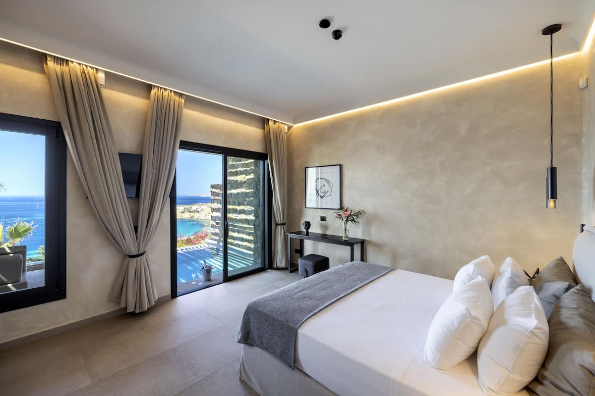 A modern bedroom with a large bed, a desk, and a view of the ocean.
