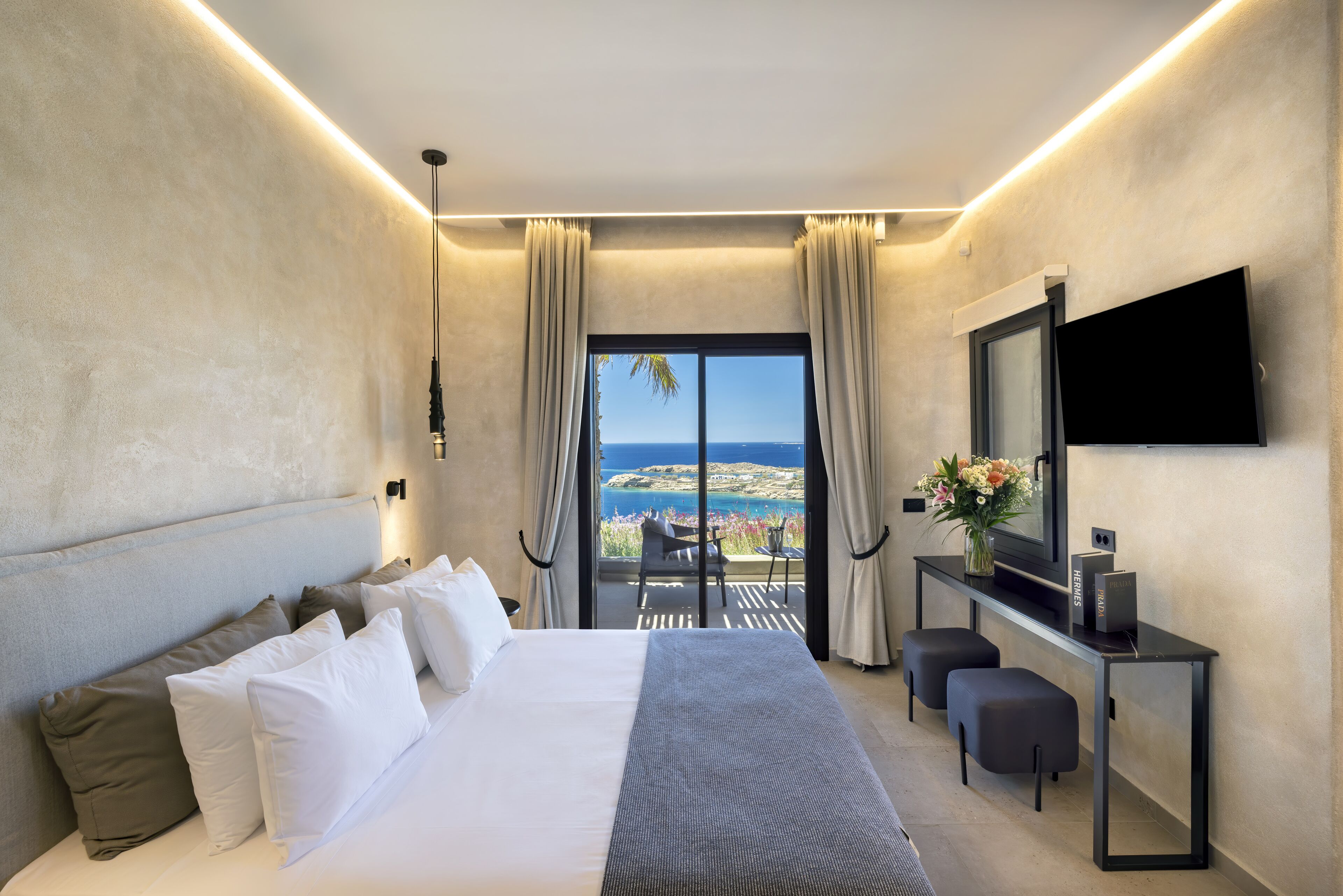 Una habitación de hotel moderna con una cama grande, un escritorio con televisión de pantalla plana y un balcón con vistas al mar.