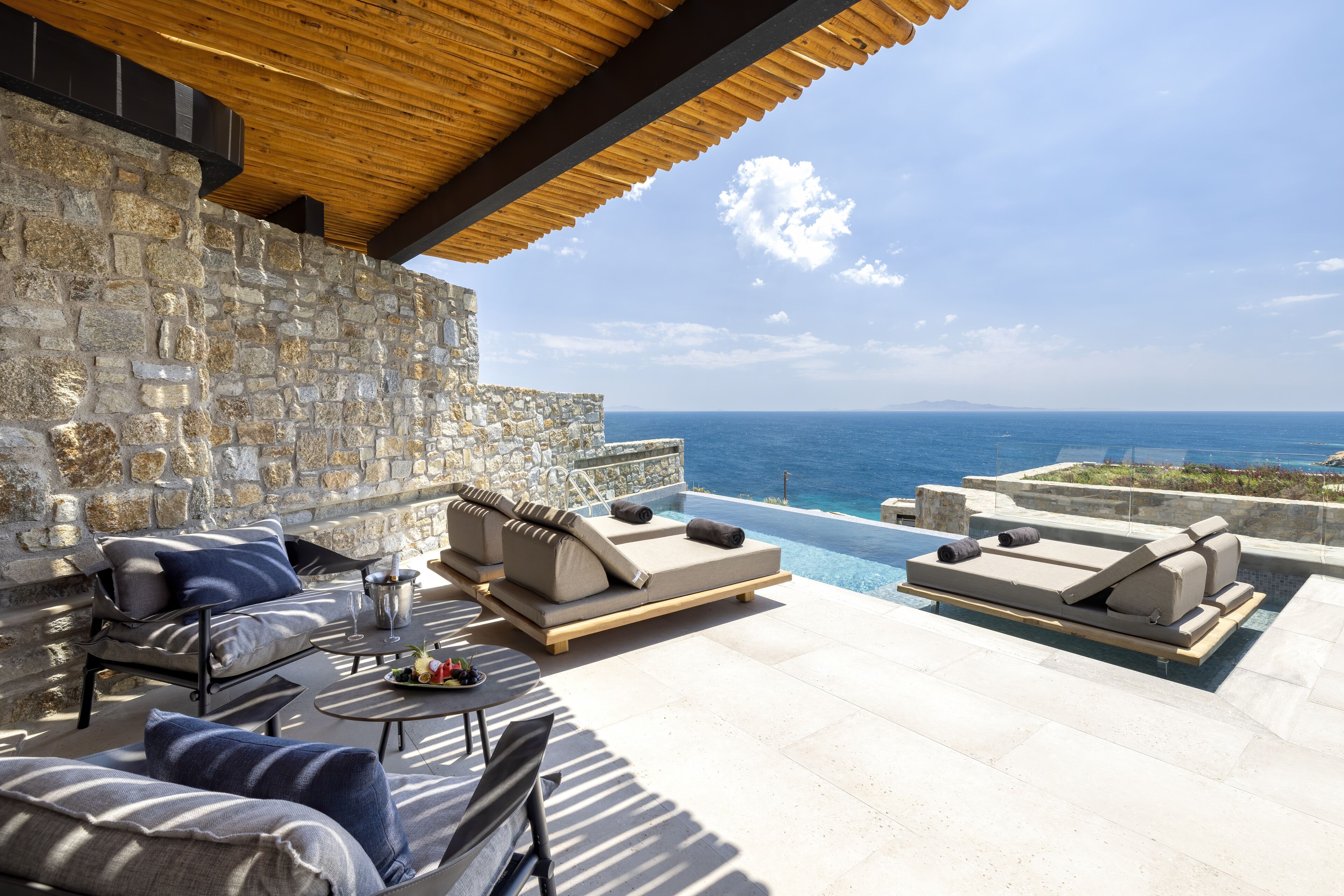 A stone-walled outdoor seating area with lounge chairs and a pool overlooking the sea.
