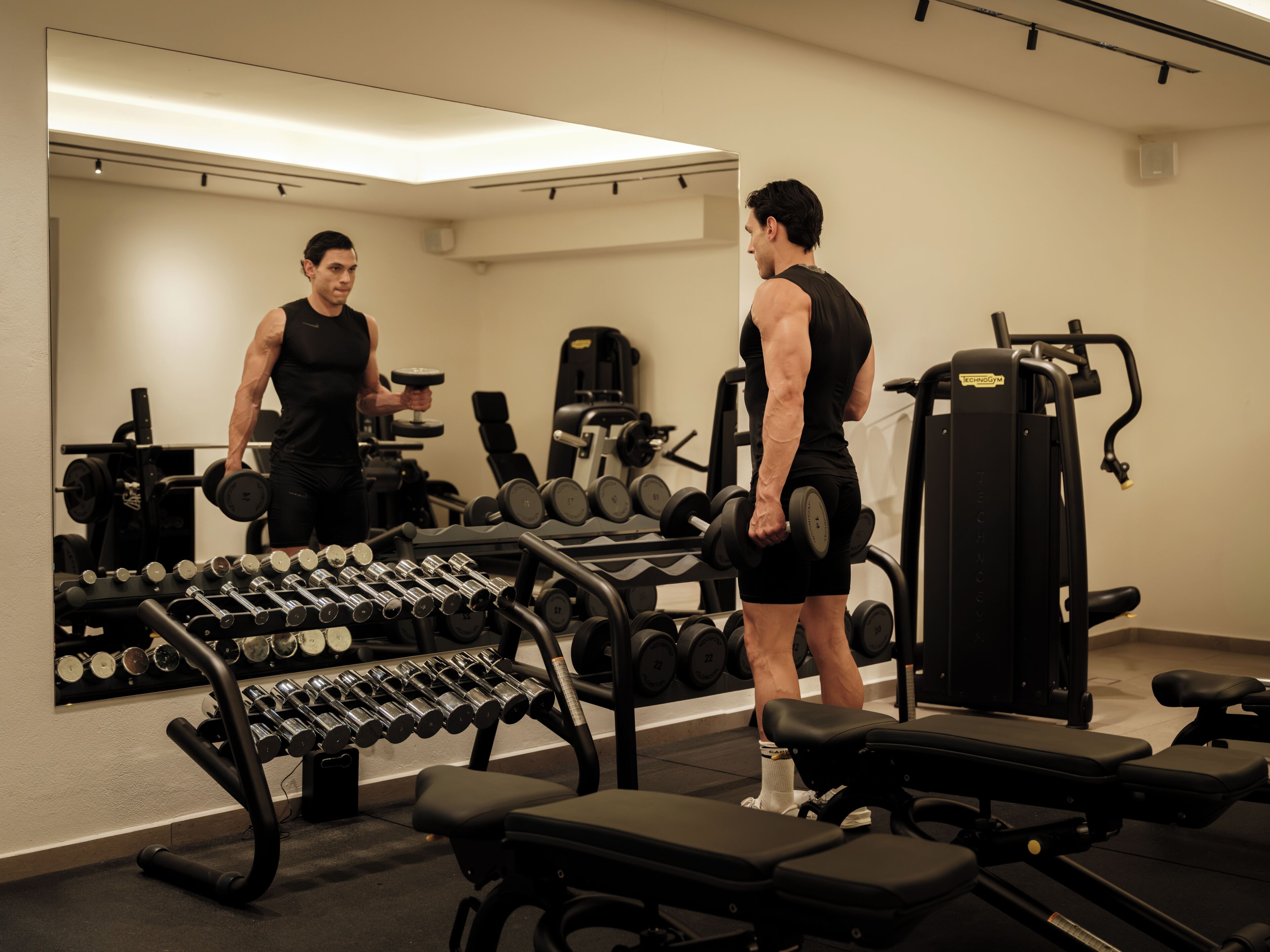 A gym with exercise equipment, benches, and a mirror.
