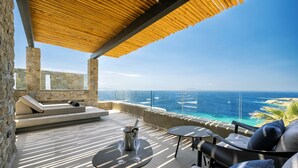 A rooftop terrace with a wooden pergola, stone walls, a cushioned seating area, and a view of the ocean. - Tropicana Suites & Villas (Mykonos)