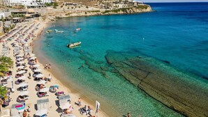 A coastal beach with clear turquoise waters, a sandy shore, and several boats. - Tropicana Suites & Villas (Mykonos)