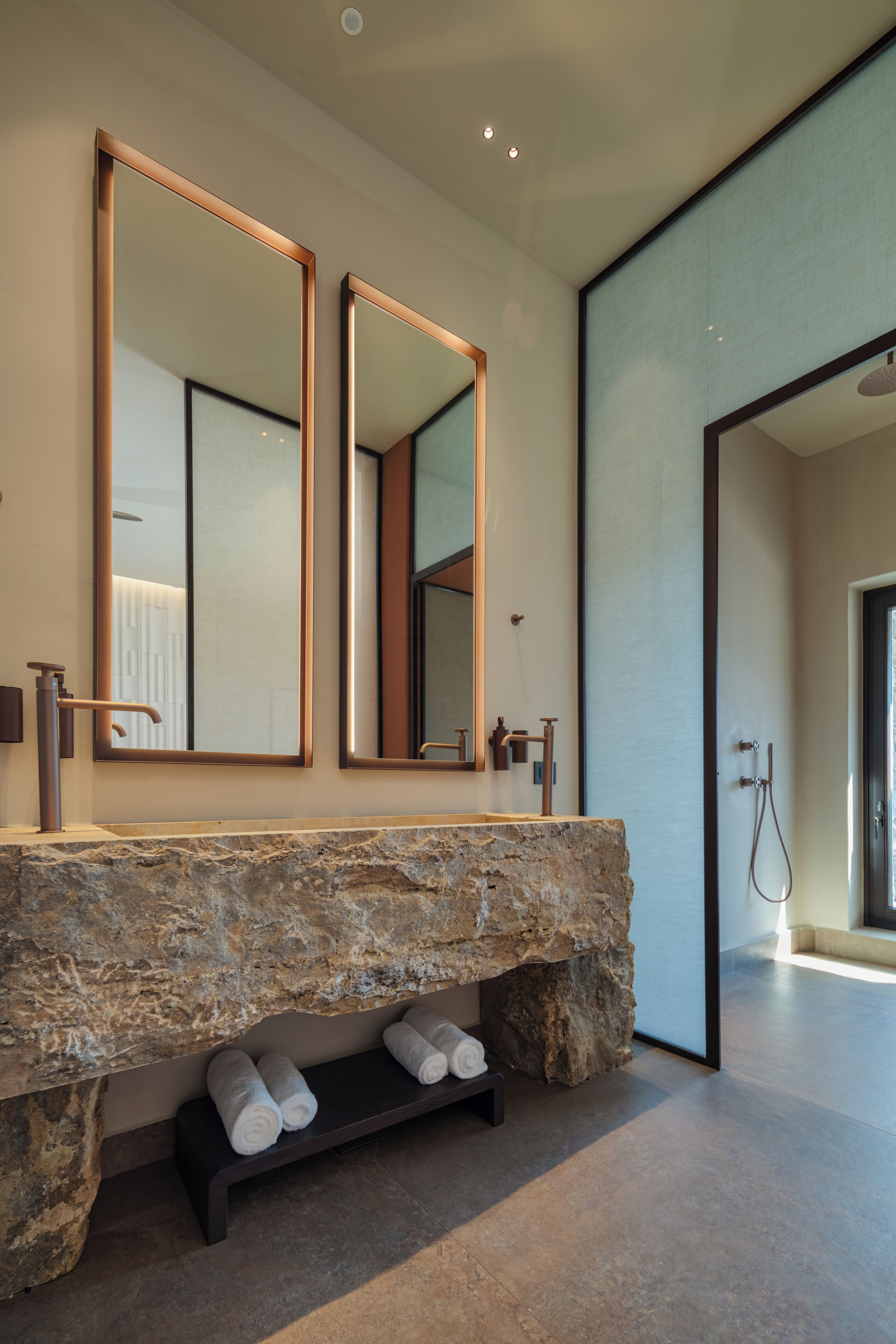Un baño moderno con un lavamanos de piedra grande, dos espejos y una zona de ducha.