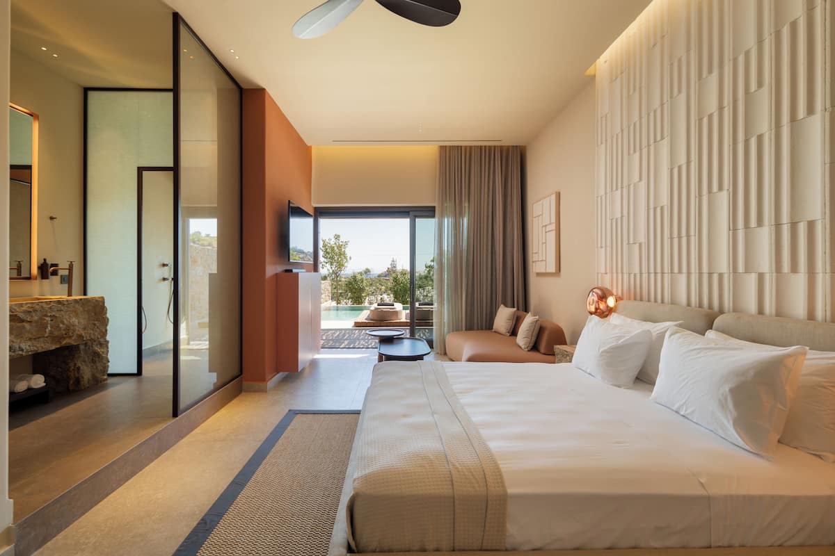 A modern hotel room with a large bed, a sofa, a TV, and a view of the outdoors.